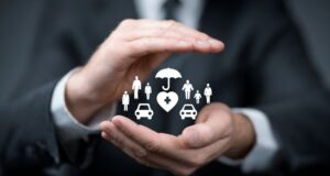 Businessperson’s hands forming a protective gesture around icons representing health, family, and car insurance